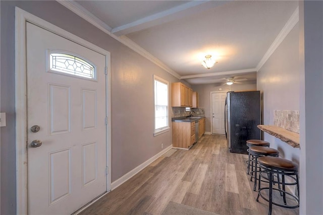 kitchen with backsplash, crown molding, sink, light hardwood / wood-style floors, and stainless steel refrigerator