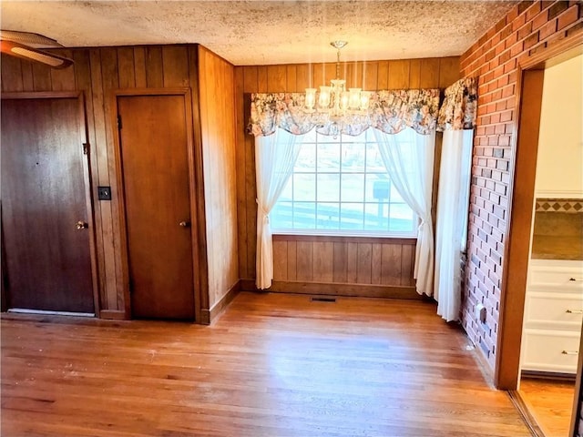 unfurnished dining area with wood walls, light wood-type flooring, a textured ceiling, and a notable chandelier