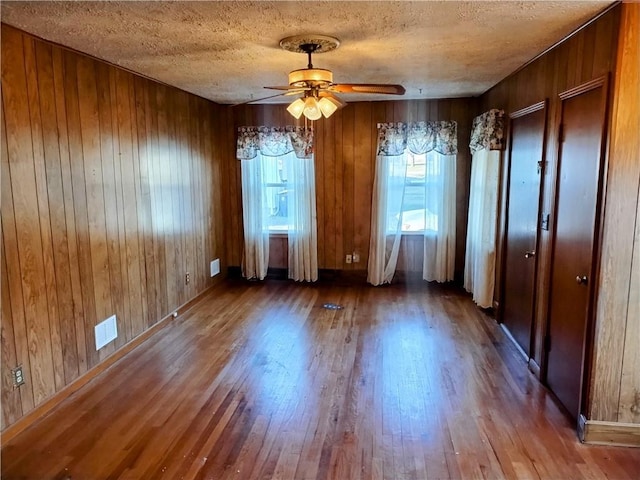 unfurnished dining area with hardwood / wood-style flooring, ceiling fan, wooden walls, and a textured ceiling