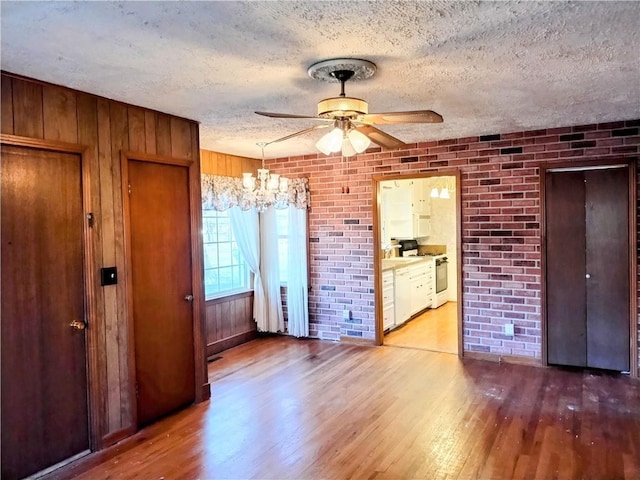 unfurnished bedroom with light wood-type flooring, ceiling fan with notable chandelier, brick wall, and a textured ceiling