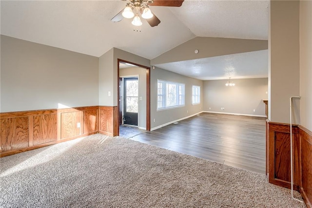 spare room with dark hardwood / wood-style floors, wood walls, ceiling fan with notable chandelier, and vaulted ceiling