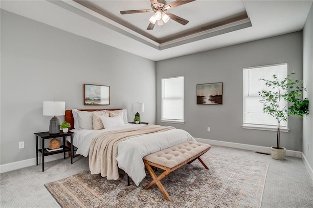 bedroom with a ceiling fan, a tray ceiling, light carpet, and baseboards