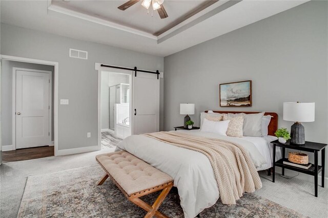 bedroom with light carpet, a barn door, a raised ceiling, and visible vents