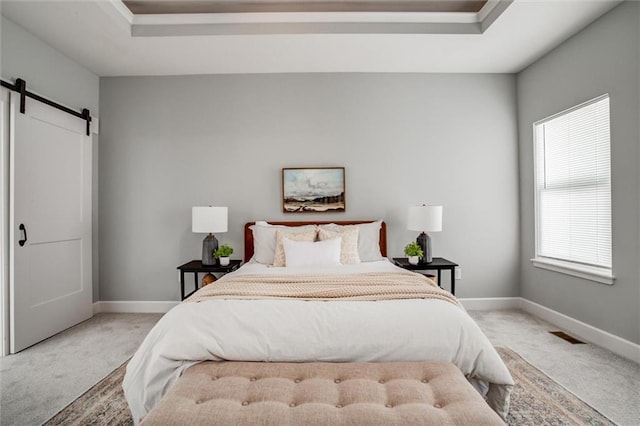 carpeted bedroom with a barn door, a raised ceiling, visible vents, and baseboards