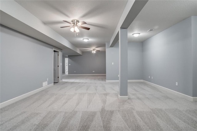 finished below grade area featuring light colored carpet, ceiling fan, visible vents, and baseboards