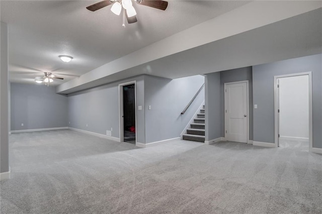 finished below grade area with light carpet, ceiling fan, stairway, and baseboards