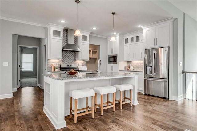 kitchen featuring a center island with sink, a sink, white cabinetry, stainless steel appliances, and wall chimney range hood