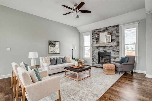 living area with dark wood-type flooring, lofted ceiling, a ceiling fan, a stone fireplace, and baseboards