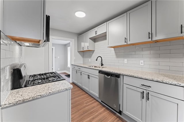 kitchen featuring dishwasher, black range, decorative backsplash, light wood-type flooring, and light stone counters