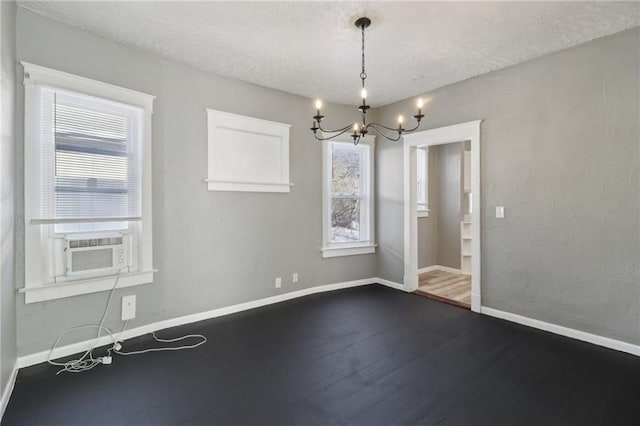 empty room with hardwood / wood-style floors, a wealth of natural light, a textured ceiling, and a chandelier