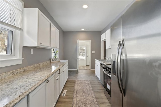 kitchen featuring white cabinets, stainless steel appliances, sink, dark hardwood / wood-style floors, and light stone counters