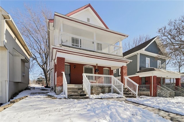 view of front of house featuring covered porch, brick siding, and a balcony