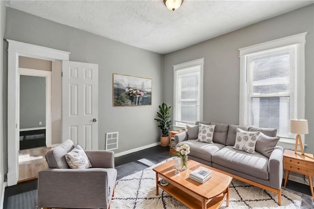 living room with a healthy amount of sunlight, baseboards, visible vents, and wood finished floors