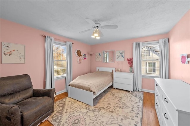 bedroom featuring multiple windows, ceiling fan, light hardwood / wood-style flooring, and a textured ceiling