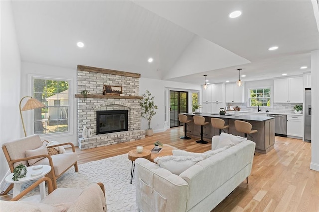 living room featuring light hardwood / wood-style floors, lofted ceiling, sink, and a brick fireplace