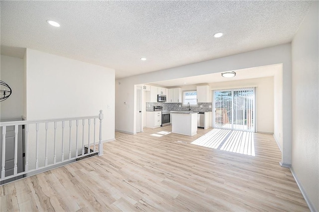 unfurnished living room with sink, light wood-type flooring, and a textured ceiling