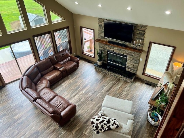 living room featuring wood-type flooring, high vaulted ceiling, and a stone fireplace