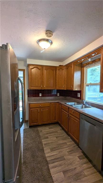 kitchen featuring decorative backsplash, a textured ceiling, stainless steel appliances, dark wood-type flooring, and sink