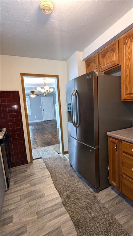 kitchen with a textured ceiling, ceiling fan with notable chandelier, light hardwood / wood-style floors, and stainless steel appliances