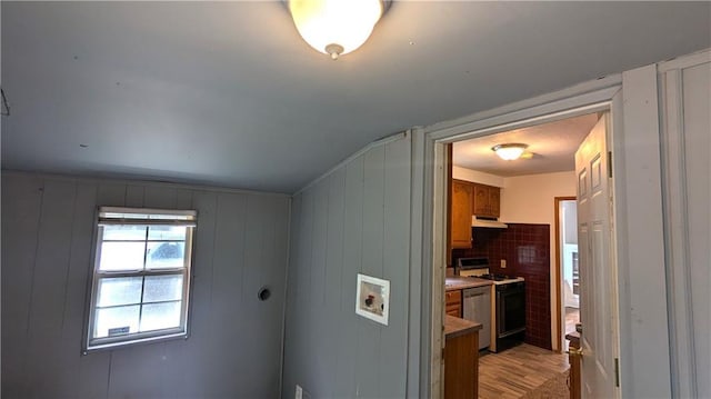 interior space with stainless steel appliances, tasteful backsplash, light hardwood / wood-style flooring, wood walls, and lofted ceiling