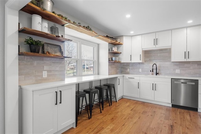 kitchen with stainless steel dishwasher, white cabinets, light wood-type flooring, and sink