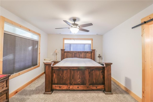 bedroom with a barn door, light colored carpet, multiple windows, and ceiling fan