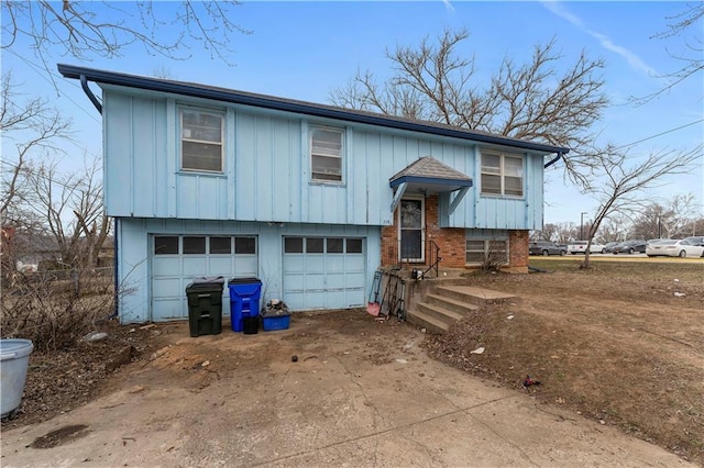 bi-level home with an attached garage, driveway, board and batten siding, and brick siding