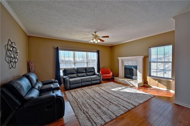 living room with ceiling fan, hardwood / wood-style floors, a textured ceiling, and a tiled fireplace