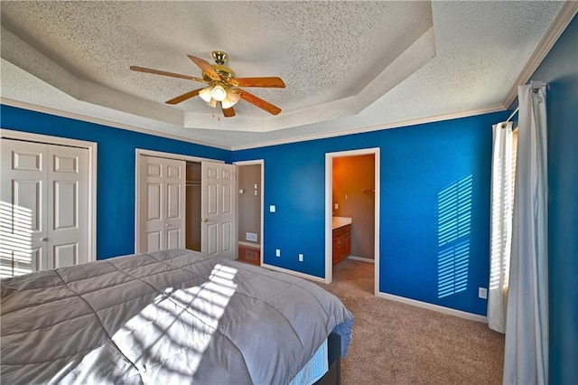 carpeted bedroom featuring a textured ceiling, connected bathroom, a raised ceiling, ceiling fan, and multiple closets