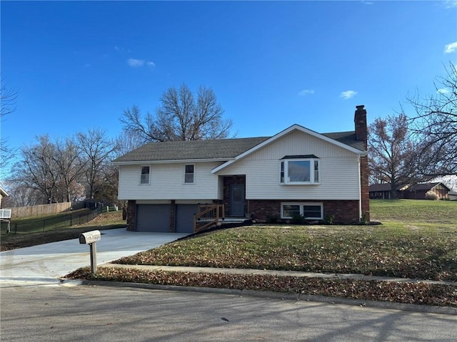 raised ranch with concrete driveway, a chimney, an attached garage, fence, and a front lawn