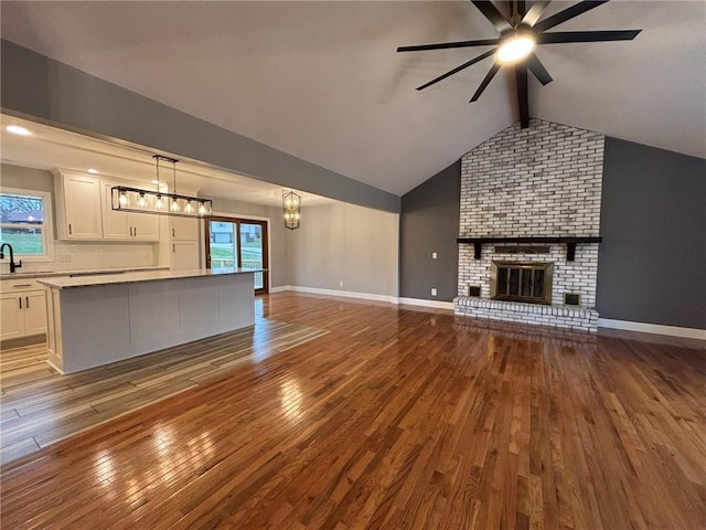 unfurnished living room featuring baseboards, hardwood / wood-style flooring, vaulted ceiling with beams, a brick fireplace, and a sink