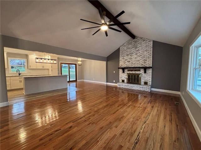 unfurnished living room featuring lofted ceiling with beams, hardwood / wood-style floors, a brick fireplace, and a sink