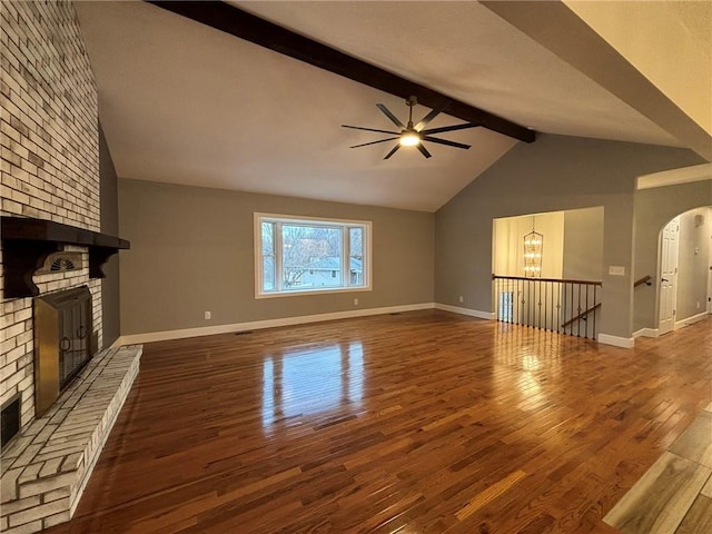 unfurnished living room with lofted ceiling with beams, a brick fireplace, wood finished floors, and baseboards