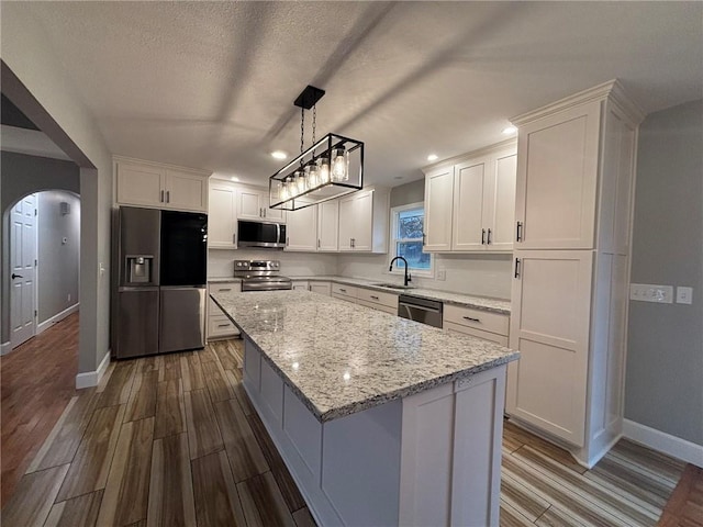 kitchen with stainless steel appliances, arched walkways, white cabinetry, and a sink