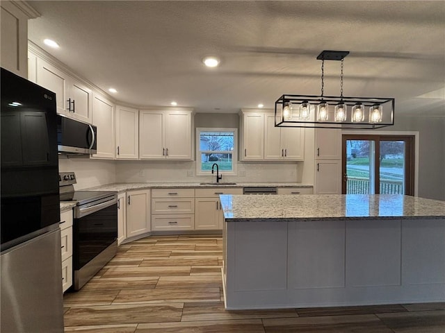 kitchen with stainless steel appliances, wood tiled floor, white cabinets, a sink, and light stone countertops