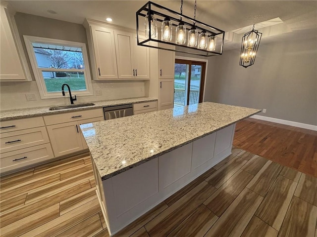 kitchen with tasteful backsplash, white cabinets, wood finished floors, a sink, and stainless steel dishwasher