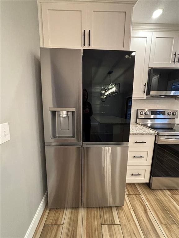 kitchen featuring light wood-style flooring, white cabinetry, baseboards, appliances with stainless steel finishes, and light stone countertops