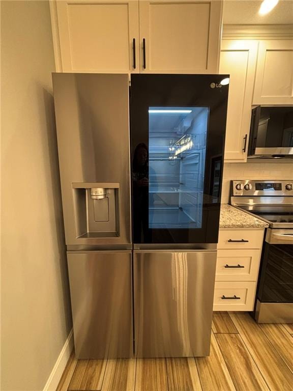 kitchen with baseboards, appliances with stainless steel finishes, light stone countertops, wood finish floors, and white cabinetry