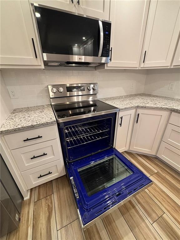 kitchen featuring light wood finished floors, stainless steel microwave, electric range, white cabinetry, and light stone countertops