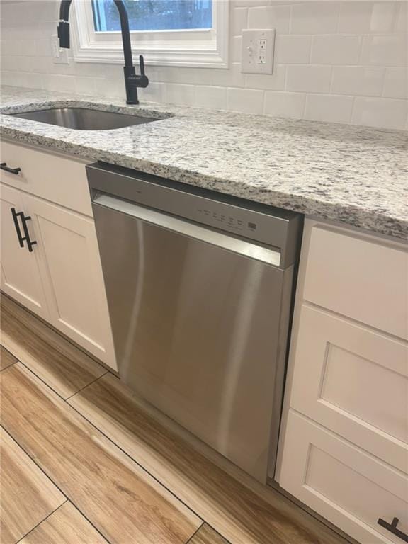 interior details with light stone counters, a sink, white cabinetry, dishwasher, and tasteful backsplash