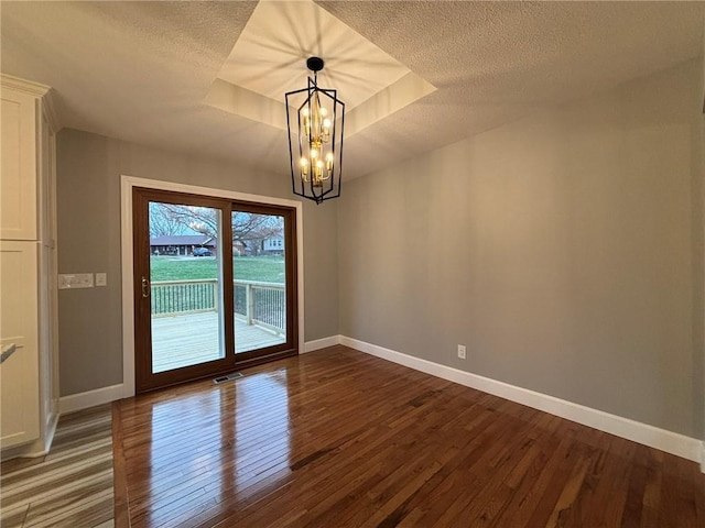 empty room featuring hardwood / wood-style flooring, baseboards, a raised ceiling, and a textured ceiling