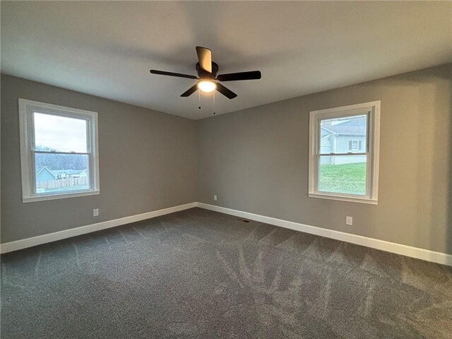 spare room with a ceiling fan, dark colored carpet, plenty of natural light, and baseboards