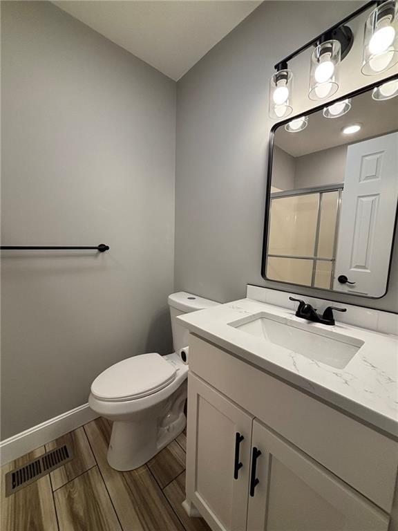 bathroom with toilet, wood finish floors, vanity, visible vents, and a shower stall