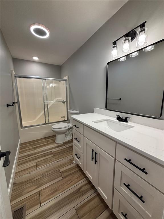 full bathroom featuring shower / bath combination with glass door, visible vents, toilet, wood tiled floor, and vanity