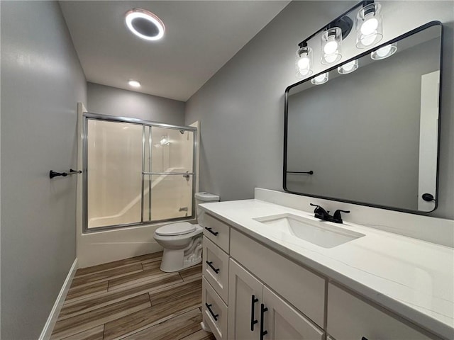 bathroom featuring toilet, wood finish floors, vanity, baseboards, and combined bath / shower with glass door