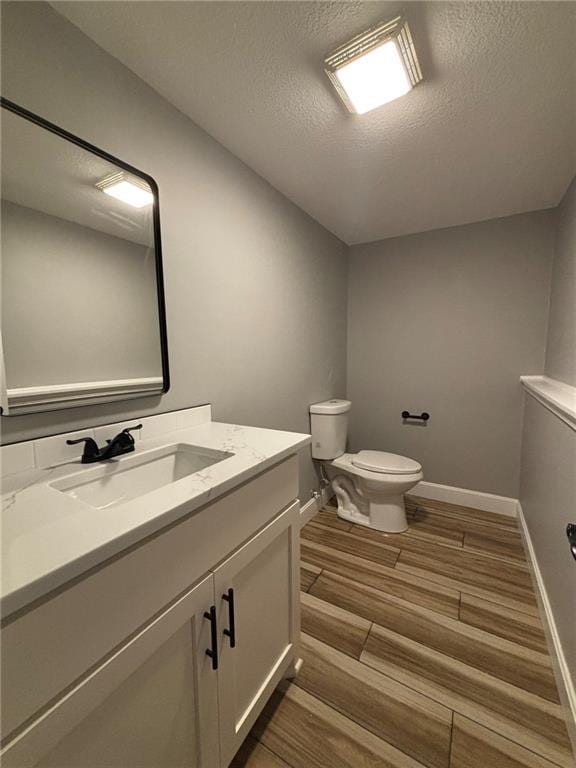 half bath with vanity, a textured ceiling, toilet, and wood finished floors