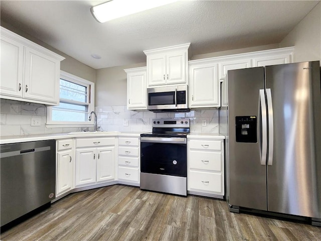 kitchen with appliances with stainless steel finishes, backsplash, sink, wood-type flooring, and white cabinets