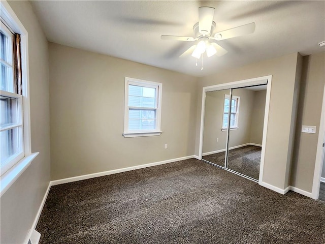 unfurnished bedroom featuring multiple windows, ceiling fan, a closet, and dark colored carpet