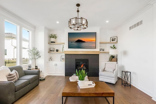 living room featuring hardwood / wood-style floors, built in features, ornamental molding, a chandelier, and a tiled fireplace