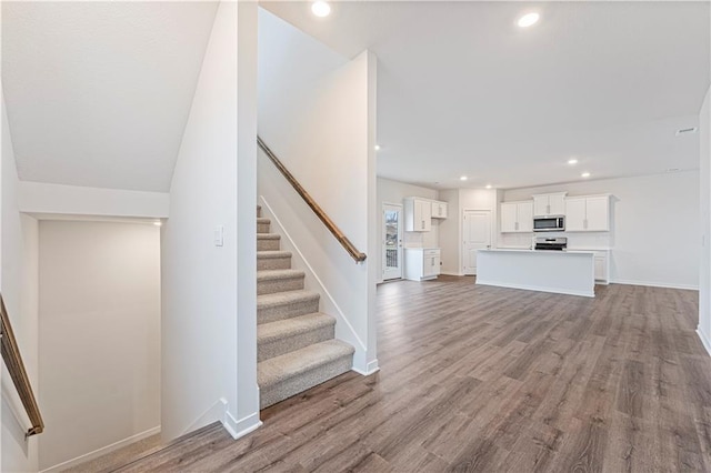 unfurnished living room with stairs, baseboards, wood finished floors, and recessed lighting